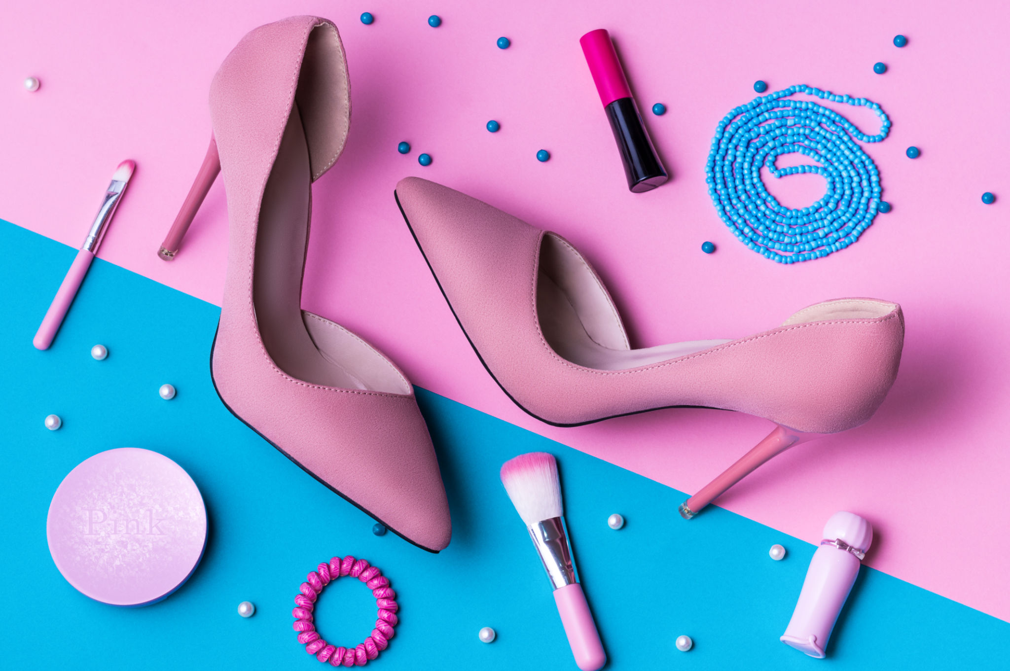 Pink Suede High Heels on pink and blue split background with accessories.
